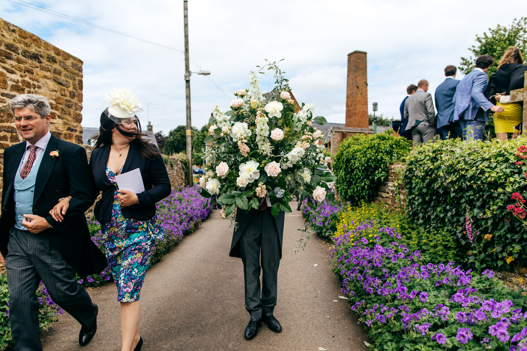 Grooms man holds massive urn of flowers and looks like some kind of flowery super hero at Farm Wedding at home 