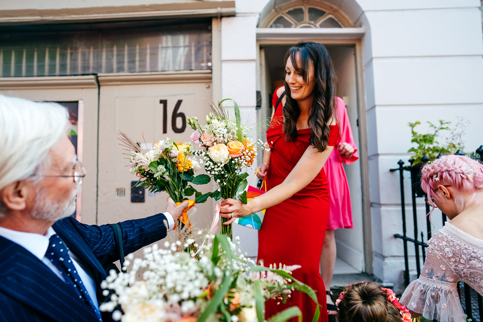 bridesmaid in red passes bouquets to bridal party london wedding