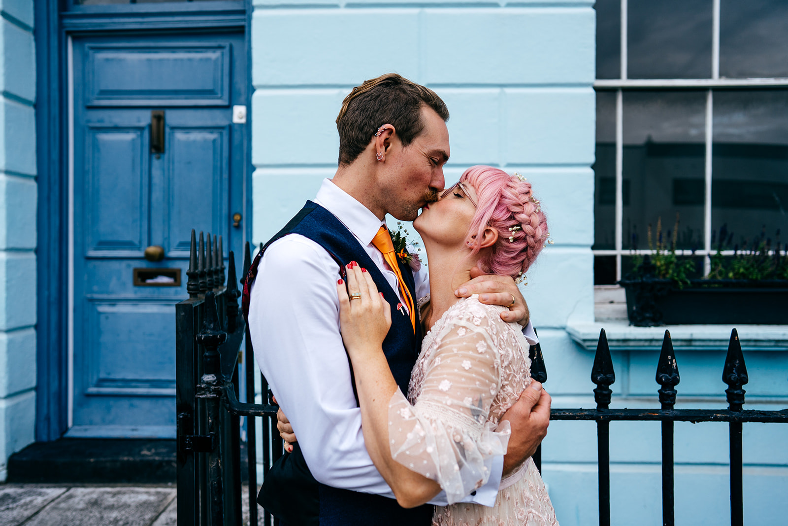 Bride with pink hair kisses groom outside baby blue house