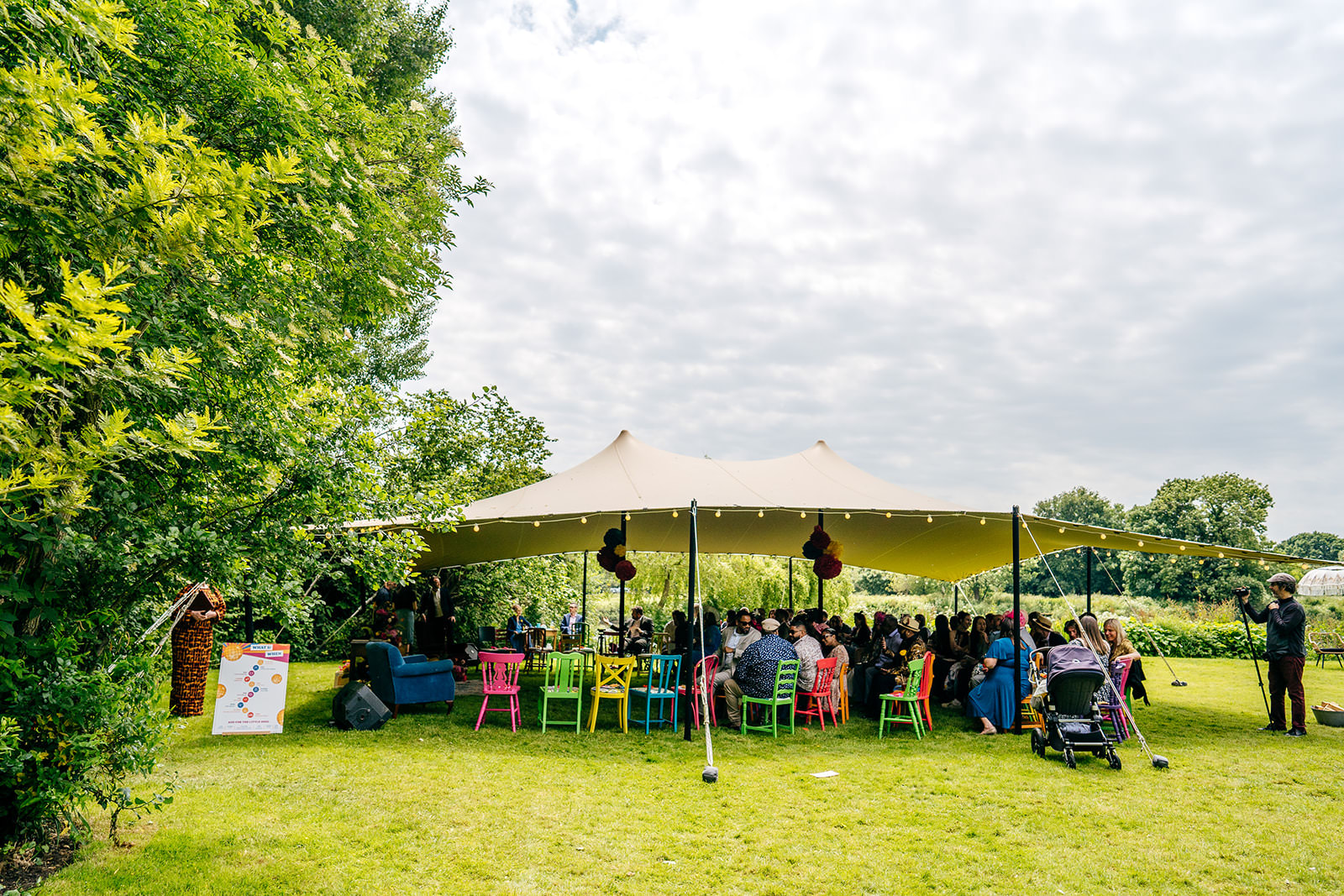 Guests waiting under canopy for arrival of the bride on colourful chairs