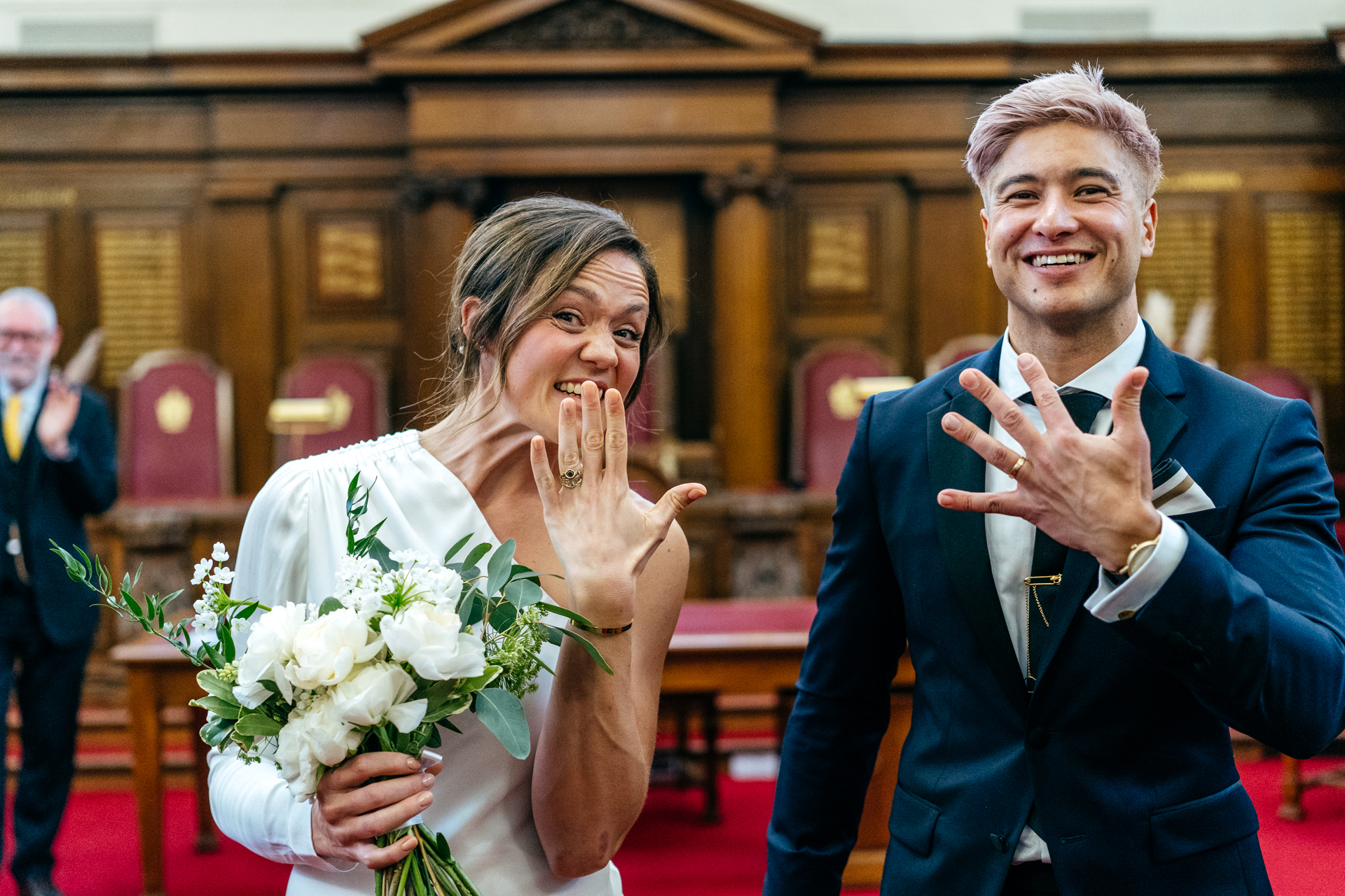 bride and groom show the photographer their rings as they walk down the aisle freshly married in Islington, London