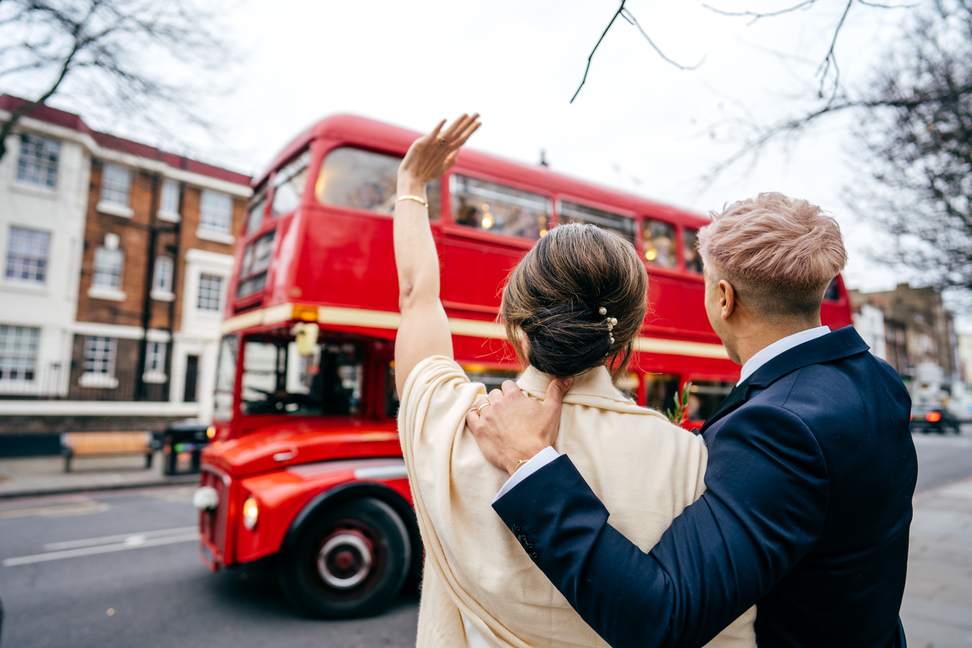 Bride and Groom waving off their wedding red London bus full of guests in London 