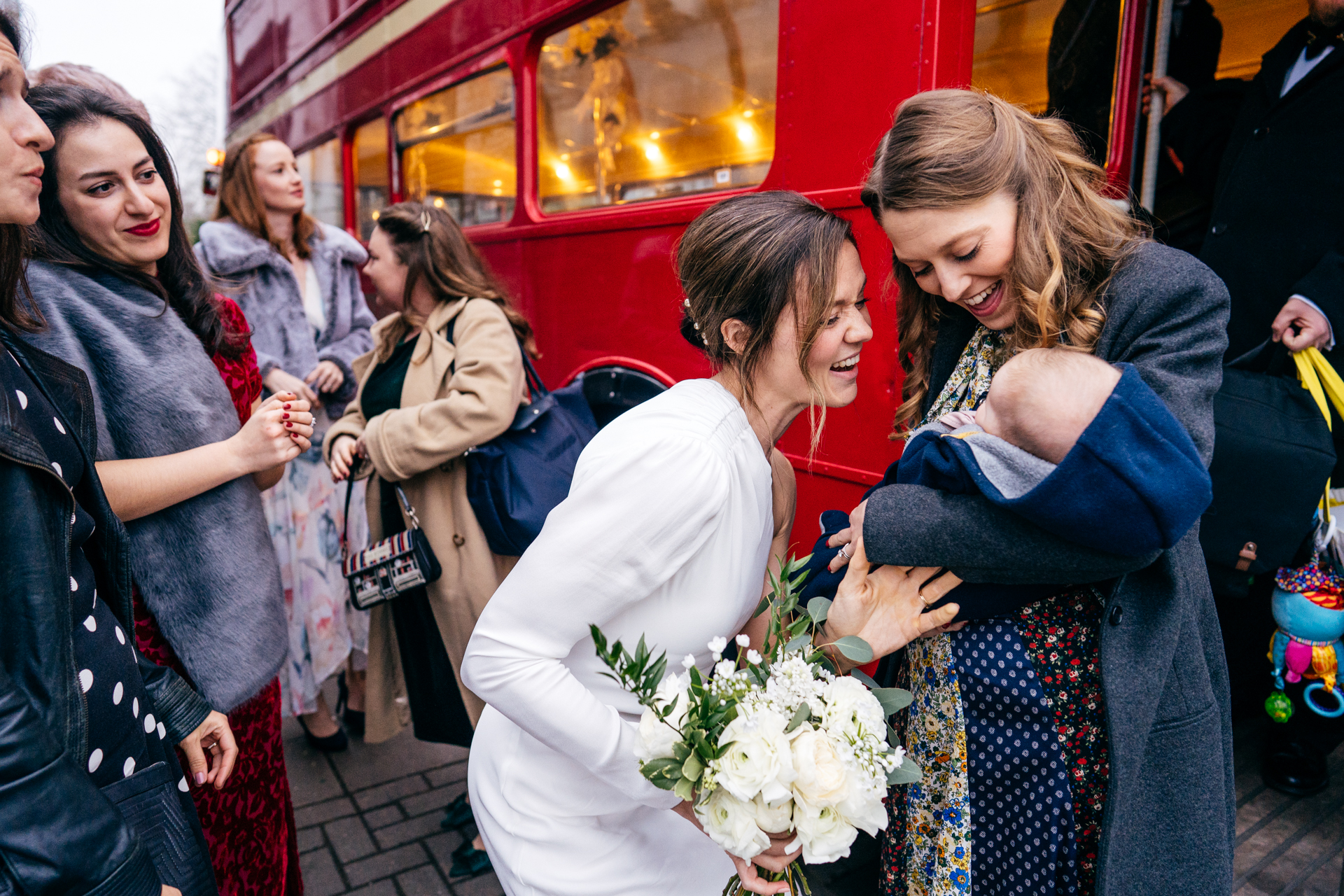 Bride greeting her guests getting off red London bus for her Clapton Country Club Wedding 