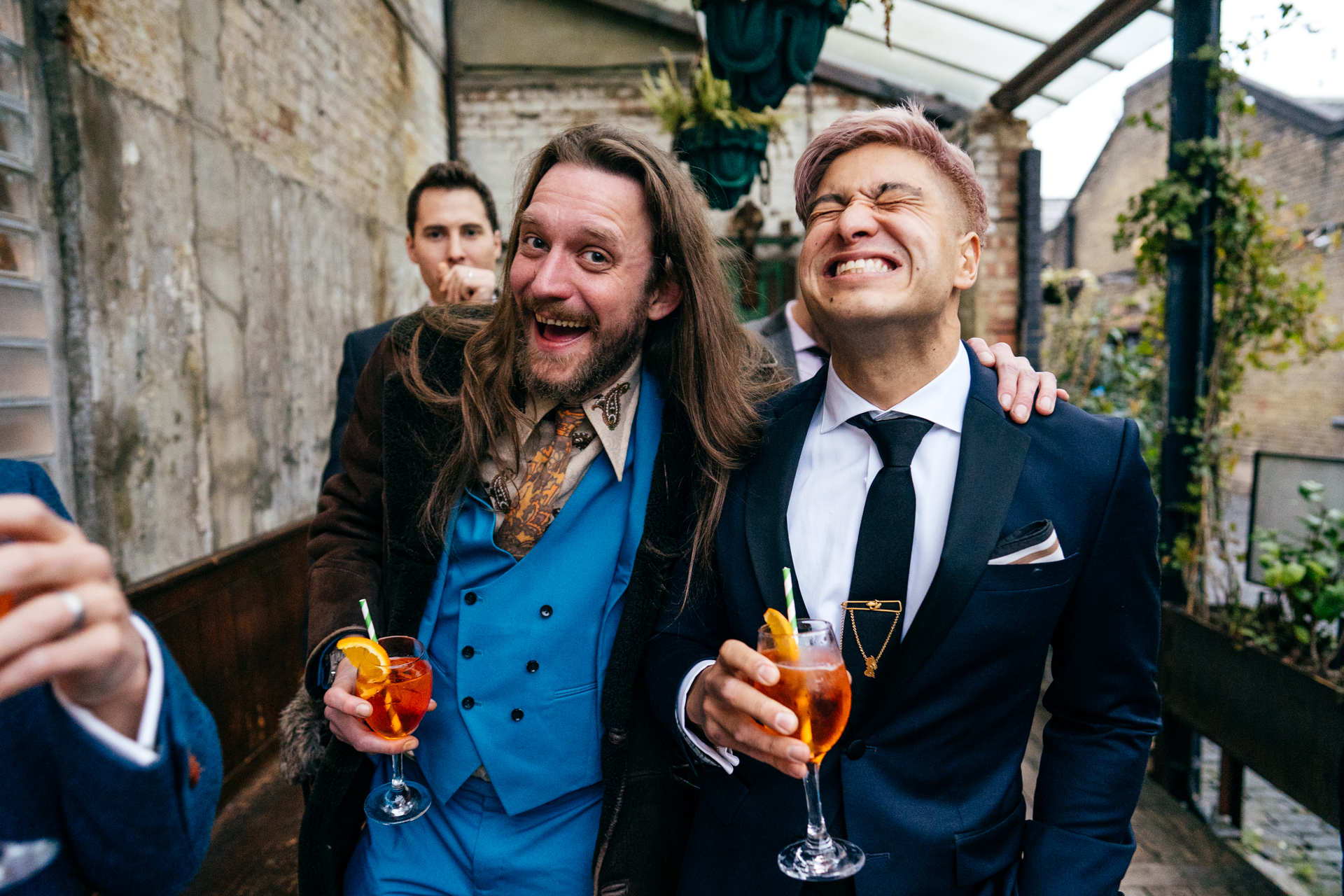 Pink haired groom does big fake smile with friend in amazing paisley vintage suit at his Clapton Country Club Wedding 
