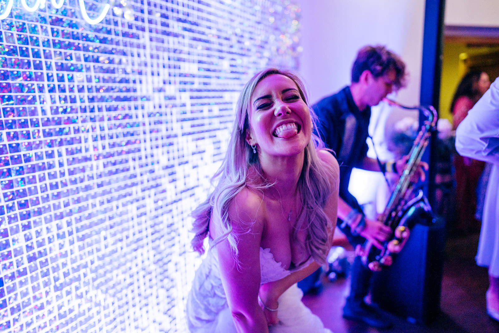 Bride in front of sparkly neon backdrop dancing with saxophonist 