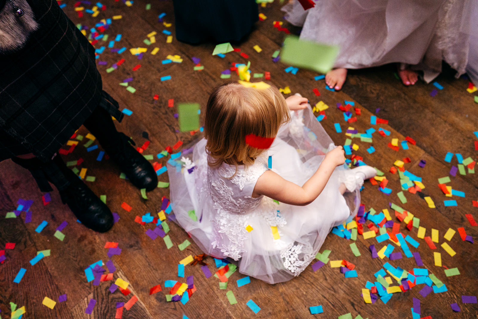 Flower girl playing with discarded confetti on dancefloor 