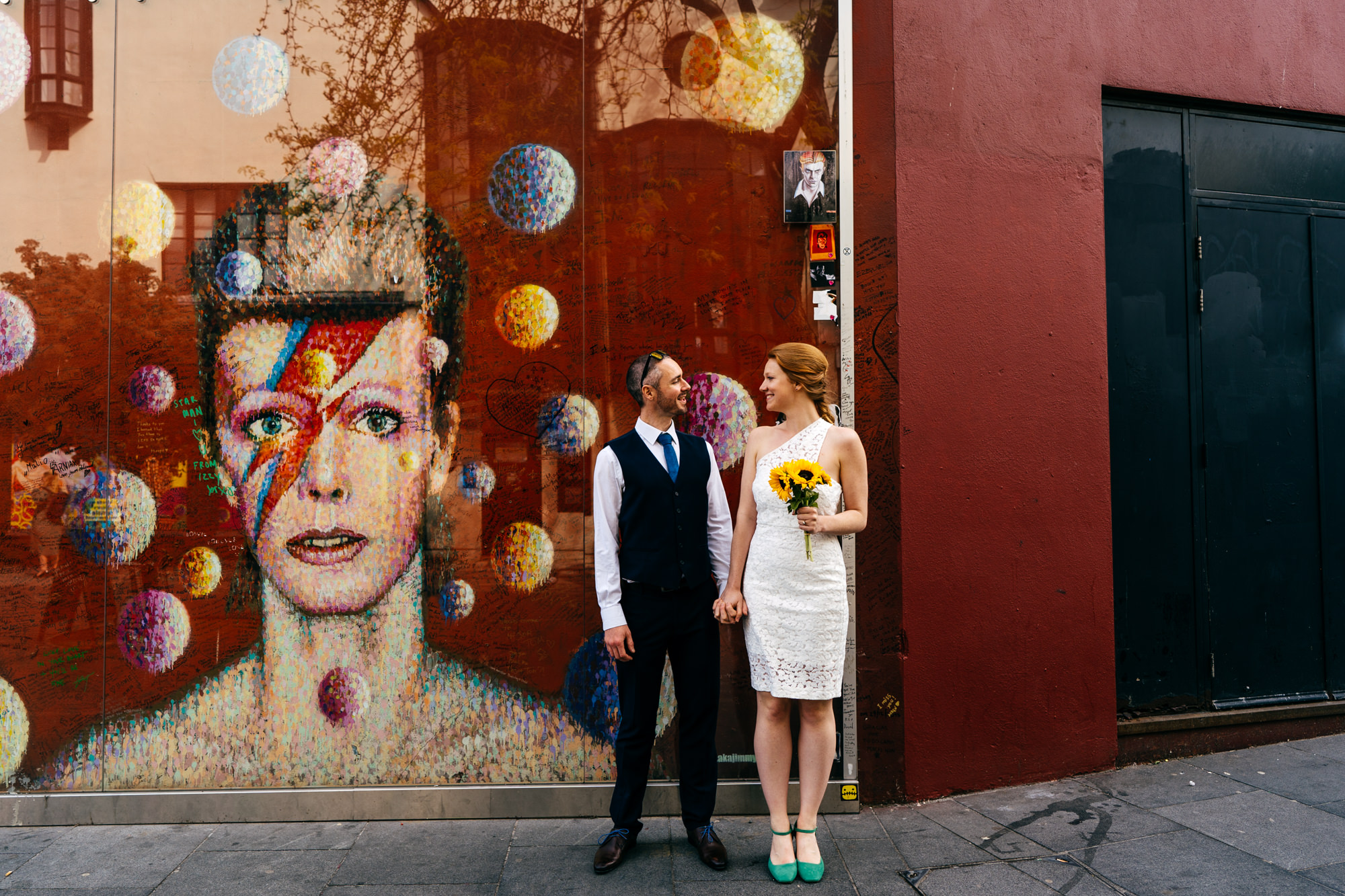 Couple in Hackney near David Bowie memorial piece. Bride wears her hair in a plait. 
