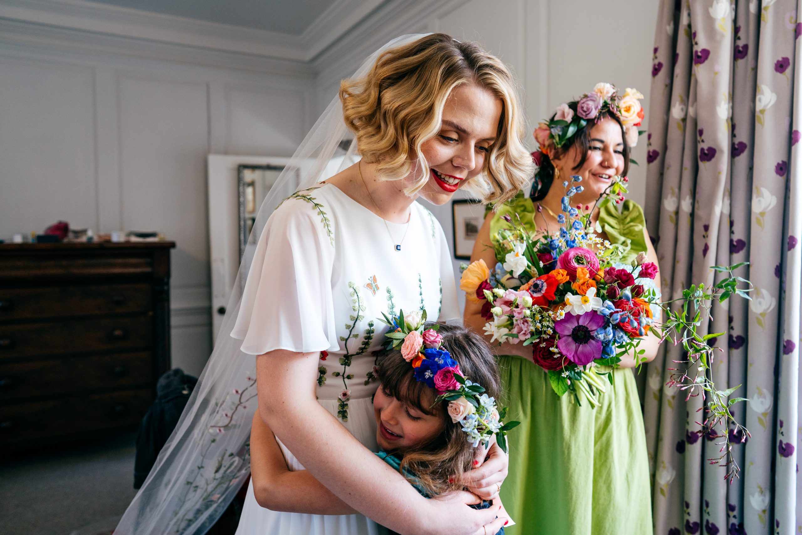 Flower girl hugs bride in beautiful embroidered dress at Sidney Sussex College. 