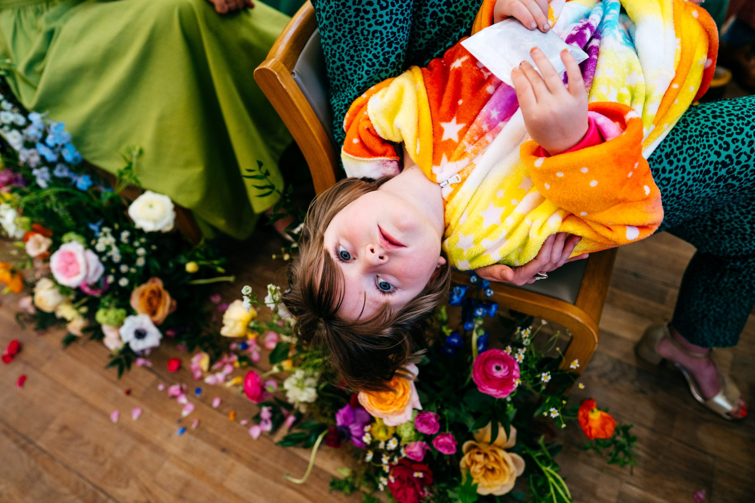 Flower girl in Unicorn outfit hangs over her mum's lap during ceremony looking bored. 