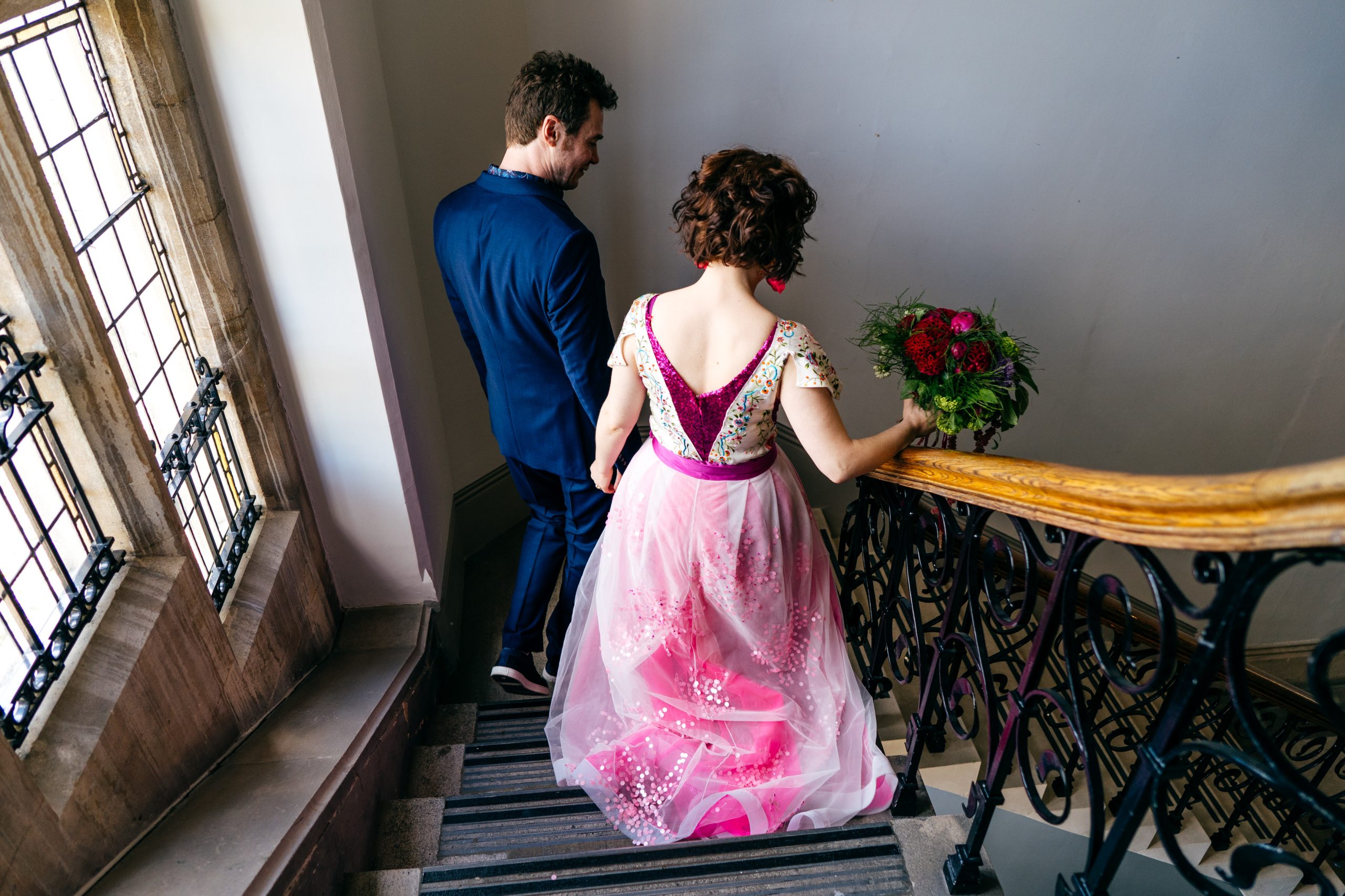 Couple exit ceremony together. Details from bride's dress can clearly be seen with layers of tulle and sequins as they go down the stairs of Winchester Town Hall. 