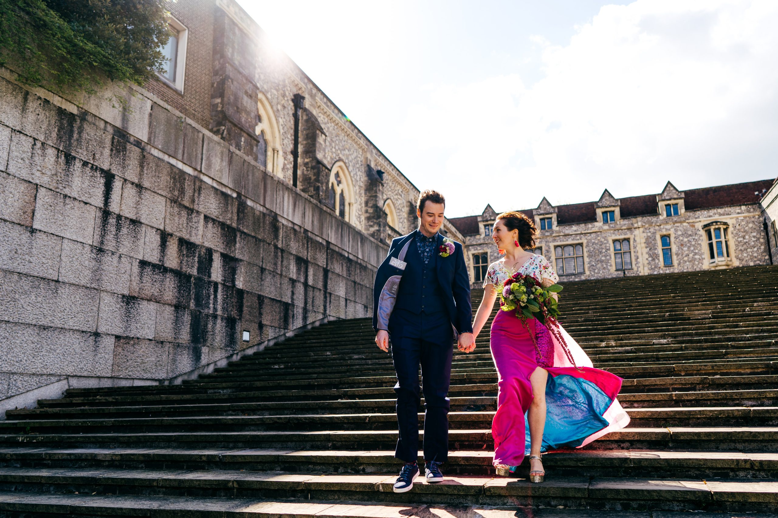 Couple walk down steps in Winchester with the sun behind them. Wind revealing the blue underskirt that clashed brilliantly with Gemma's pink skirt. 