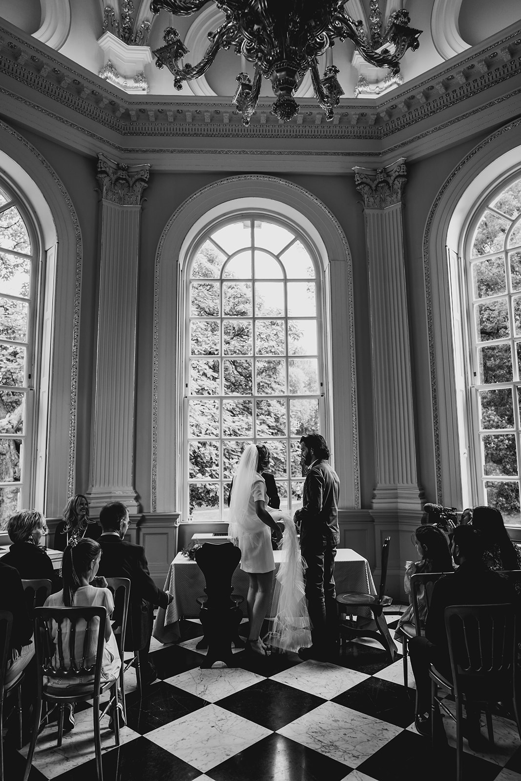 Super stylish couple exchange vows in front of huge windows of Orleans House. Bride wears short wedding dress by Gillian Million.