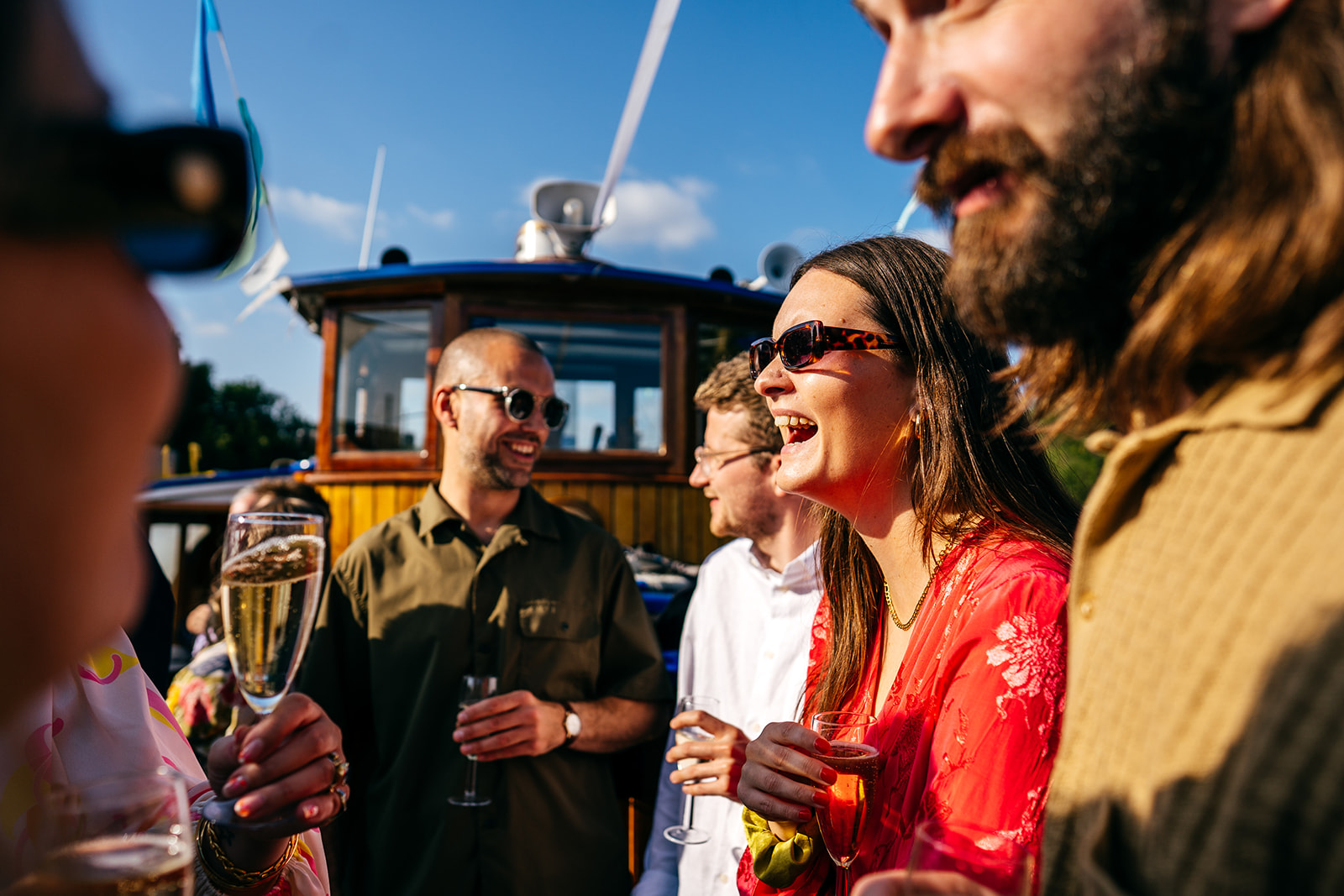 Guests laughing and sharing drinks and chat aboard boat at London Wedding.