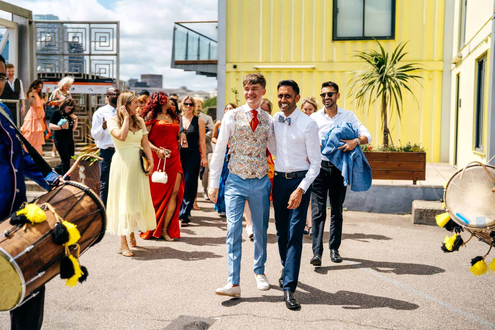 Couple disembark boat at Trinity Buoy Wharf ahead of their Humanist Ceremony. Couple and crowd dancing to dhol drummers 