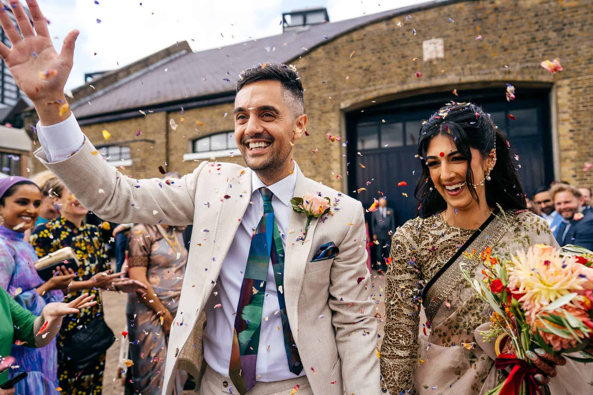 Couple during confetti at Trinity Buoy Wharf. Sikh bride wears beautiful green and gold sari. 